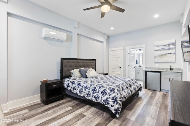 bedroom with stainless steel fridge, light wood finished floors, baseboards, a wall unit AC, and ensuite bathroom