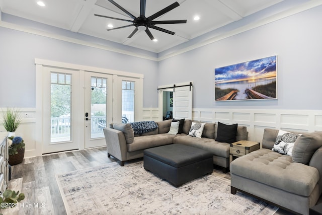 living room featuring coffered ceiling, ceiling fan, a barn door, wood finished floors, and a decorative wall