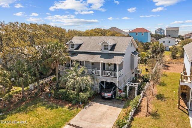 1613 E Pelican Dr, Oak Island, NC 28465 - view of front of home with concrete driveway, a carport, covered porch, roof with shingles, and a residential view