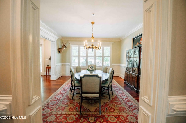 dining room with crown molding, wainscoting, dark wood-type flooring, and a notable chandelier