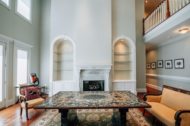 living area featuring built in features, a high ceiling, baseboards, and wood finished floors