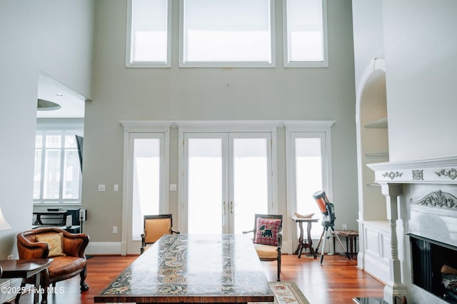 living area with wood finished floors, french doors, a high end fireplace, and a towering ceiling