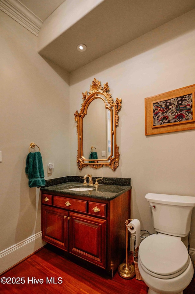 half bathroom with vanity, wood finished floors, toilet, baseboards, and recessed lighting