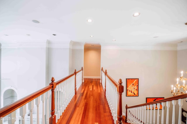 hall featuring light wood-style floors, ornamental molding, a chandelier, and an upstairs landing