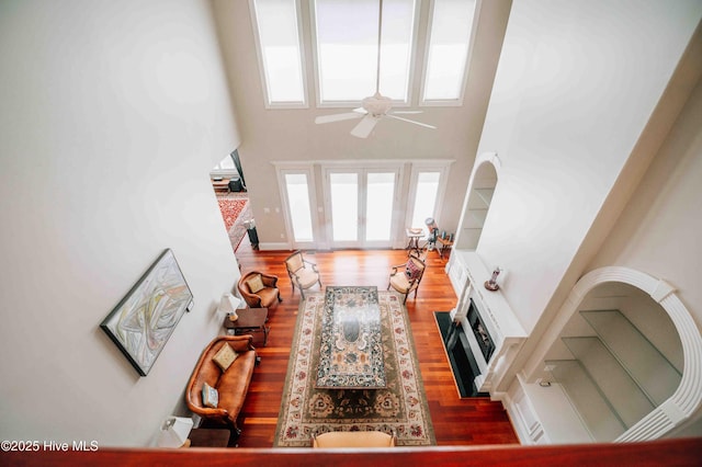 living room featuring a fireplace with flush hearth, a high ceiling, ceiling fan, and wood finished floors