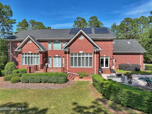 rear view of property with brick siding, roof mounted solar panels, french doors, a patio, and a yard