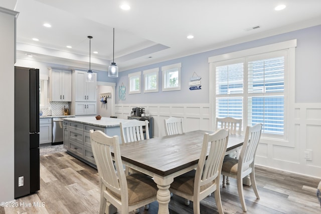 dining room with crown molding, wainscoting, light wood-style flooring, and a decorative wall