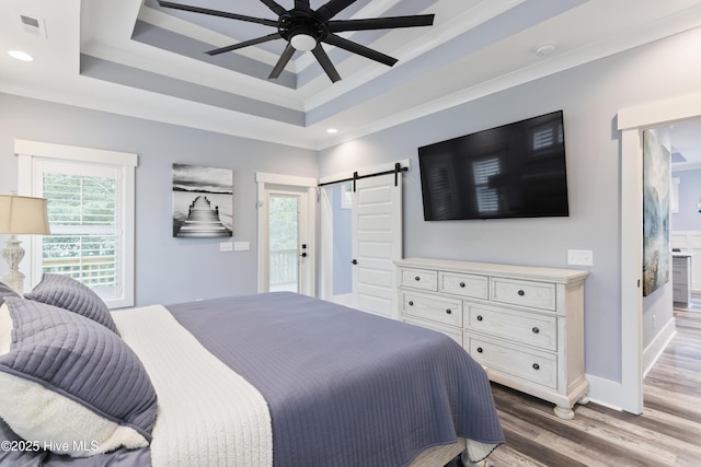 bedroom featuring a tray ceiling, recessed lighting, a barn door, and wood finished floors