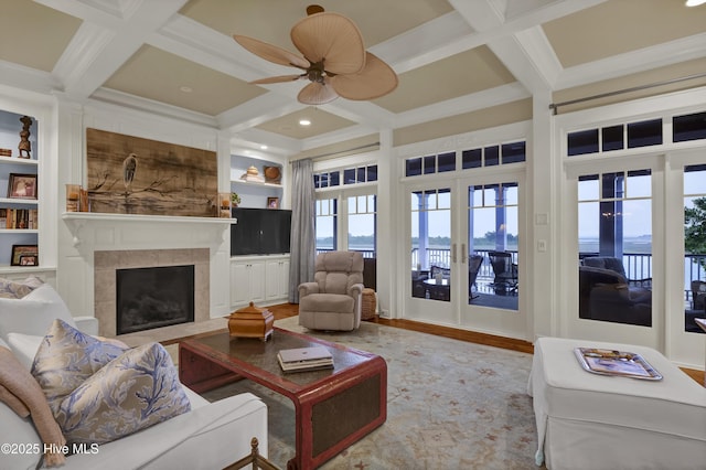 living room featuring ceiling fan, built in shelves, a fireplace with flush hearth, wood finished floors, and coffered ceiling