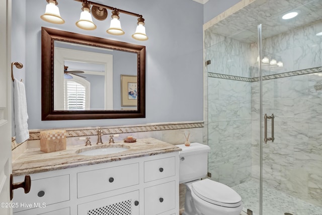 bathroom featuring wainscoting, vanity, toilet, a marble finish shower, and tile walls