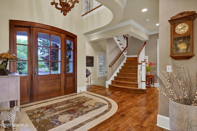 entryway with an inviting chandelier, recessed lighting, wood finished floors, ornamental molding, and stairway