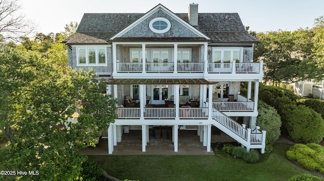 rear view of house featuring french doors, a chimney, stairway, a balcony, and a yard