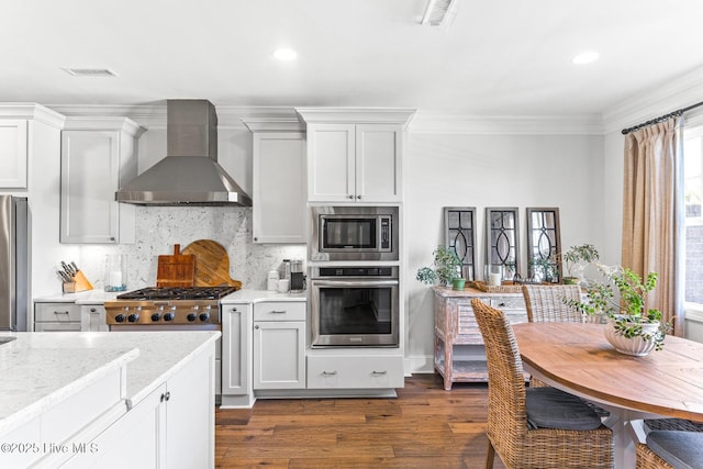 kitchen featuring visible vents, dark wood-style flooring, wall chimney range hood, backsplash, and stainless steel appliances