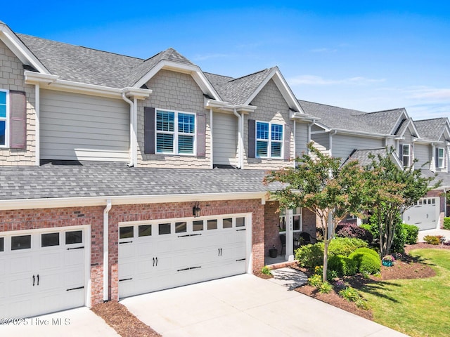 view of property featuring an attached garage, a shingled roof, driveway, and brick siding