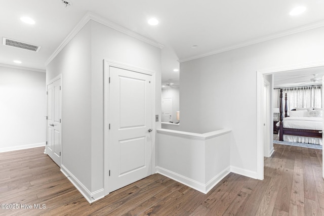 hallway featuring visible vents, ornamental molding, wood finished floors, baseboards, and recessed lighting