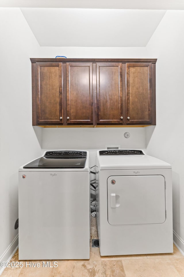 clothes washing area with washing machine and clothes dryer, baseboards, and cabinet space