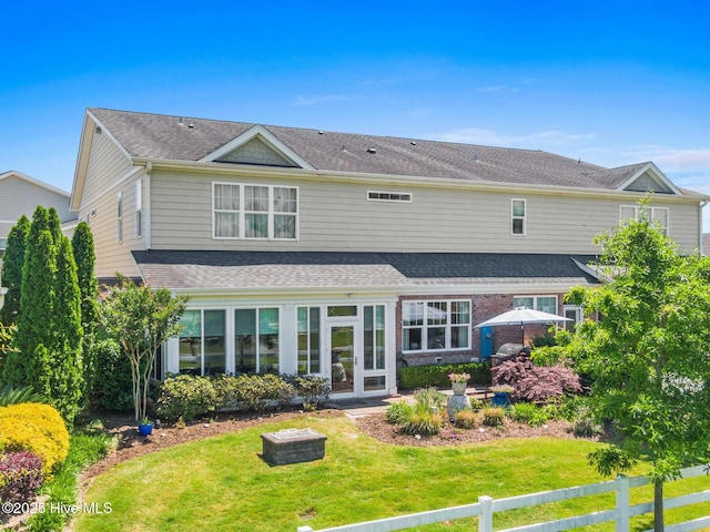 back of property featuring a lawn, roof with shingles, and fence