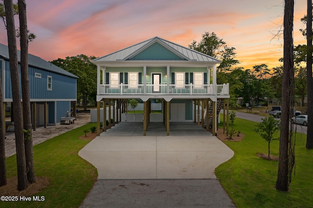coastal inspired home with a porch, concrete driveway, a standing seam roof, a carport, and a yard
