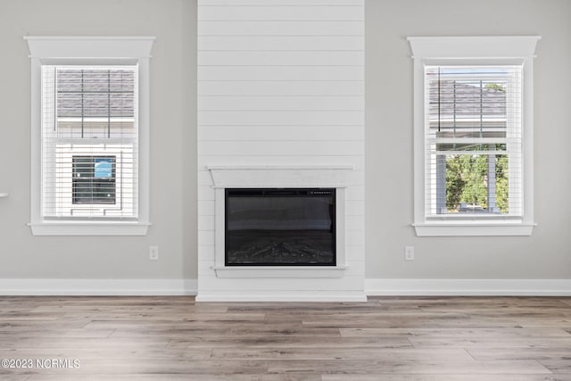 unfurnished living room with a healthy amount of sunlight, a glass covered fireplace, and wood finished floors