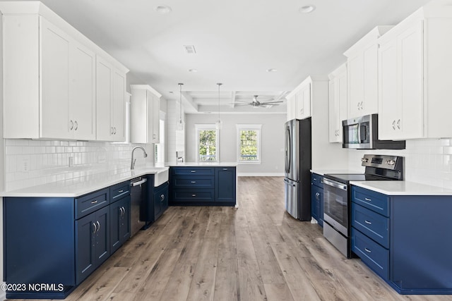 kitchen with a sink, a peninsula, light wood-type flooring, blue cabinets, and appliances with stainless steel finishes