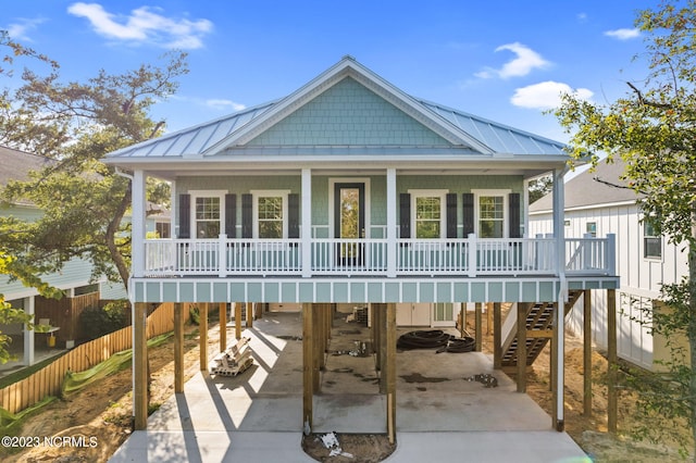 coastal inspired home featuring covered porch, driveway, a carport, stairway, and fence