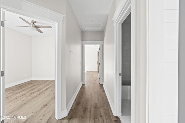 hall featuring baseboards, attic access, and wood finished floors