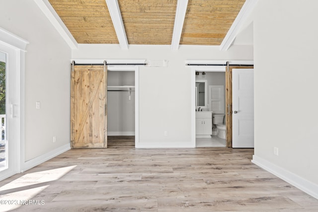 unfurnished bedroom featuring ensuite bathroom, baseboards, vaulted ceiling with beams, a barn door, and wooden ceiling