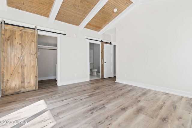unfurnished bedroom with a barn door, wood finished floors, baseboards, connected bathroom, and vaulted ceiling with beams