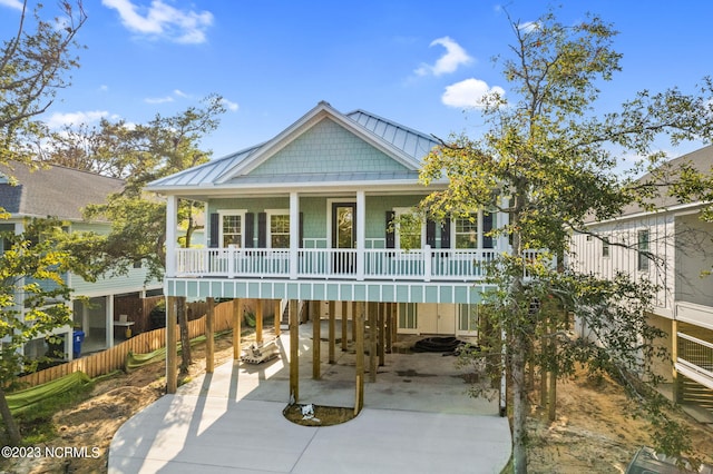 coastal inspired home with covered porch, a standing seam roof, driveway, a carport, and fence