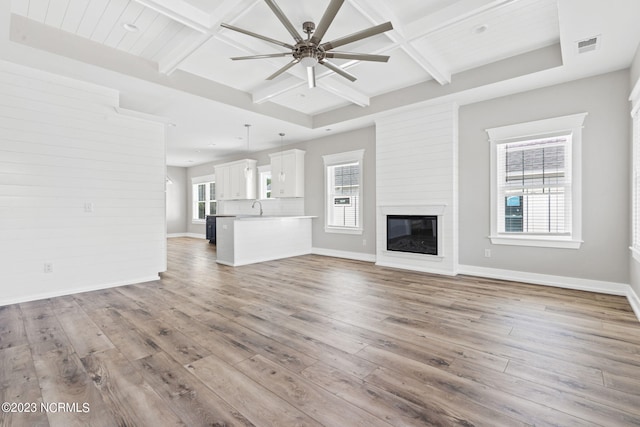 unfurnished living room with a sink, a ceiling fan, hardwood / wood-style flooring, and beam ceiling
