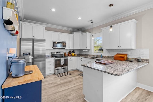 kitchen featuring a peninsula, a sink, light wood-type flooring, appliances with stainless steel finishes, and ornamental molding
