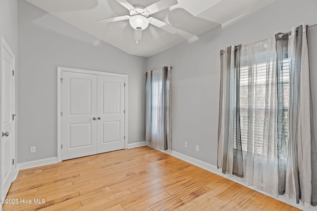 unfurnished bedroom with light wood finished floors, vaulted ceiling, baseboards, a closet, and a ceiling fan