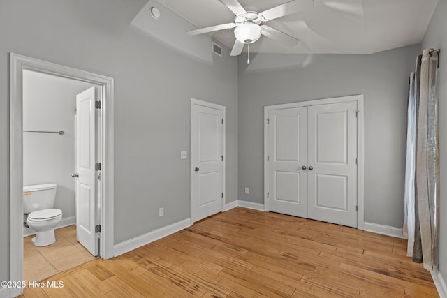 unfurnished bedroom featuring light wood-style flooring, baseboards, ensuite bathroom, ceiling fan, and a closet