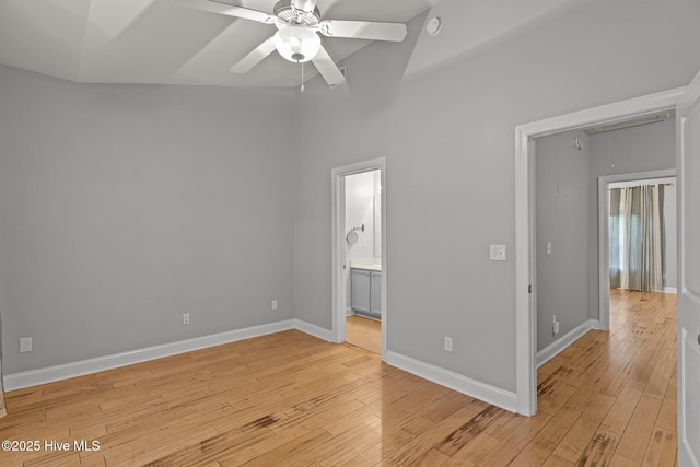 unfurnished bedroom featuring attic access, light wood finished floors, baseboards, connected bathroom, and a towering ceiling