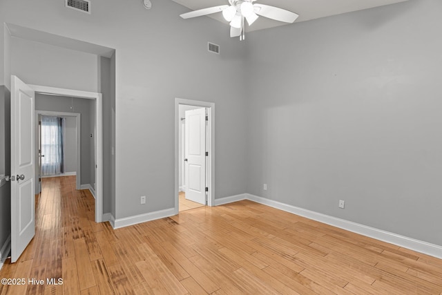 unfurnished bedroom featuring baseboards, light wood-type flooring, a towering ceiling, a ceiling fan, and ensuite bathroom