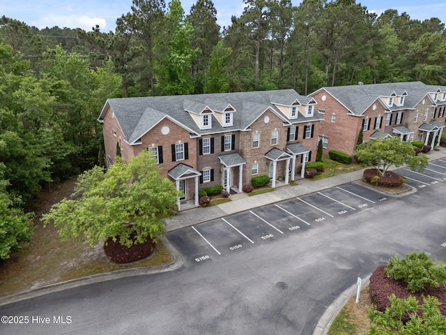 view of front of house with uncovered parking, a forest view, and brick siding