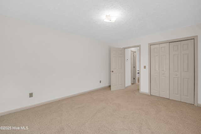 unfurnished bedroom featuring a textured ceiling, baseboards, light colored carpet, and a closet