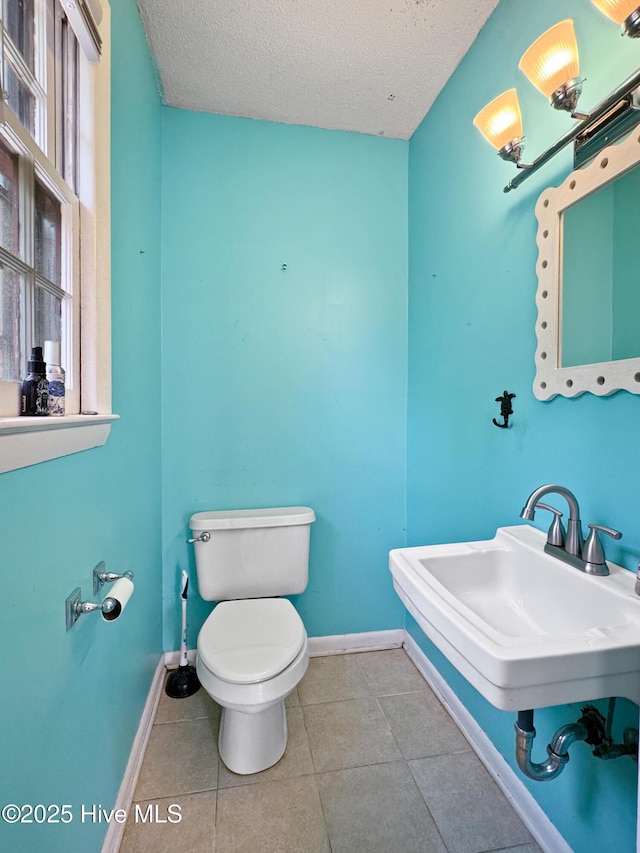 bathroom featuring a textured ceiling, toilet, tile patterned floors, and baseboards