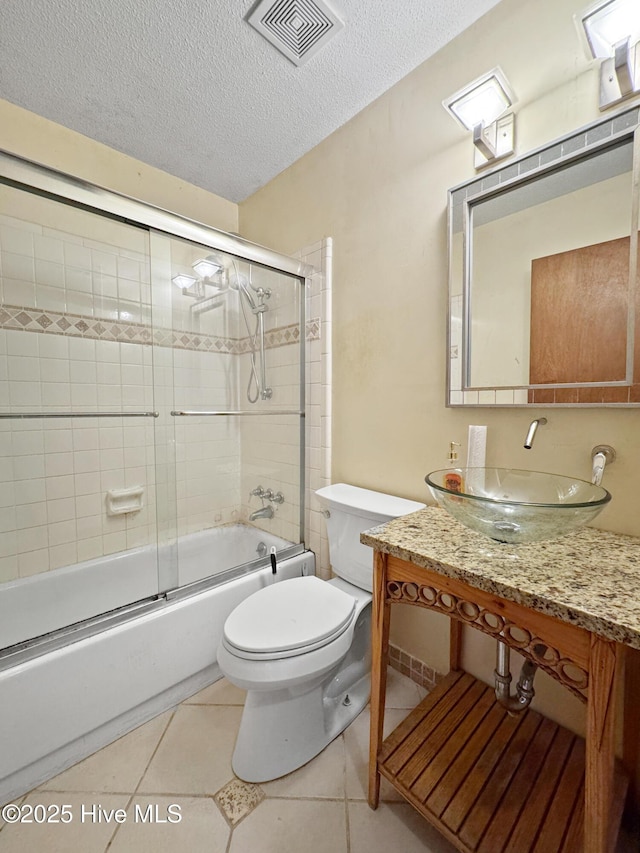 bathroom with toilet, a textured ceiling, combined bath / shower with glass door, vanity, and tile patterned flooring