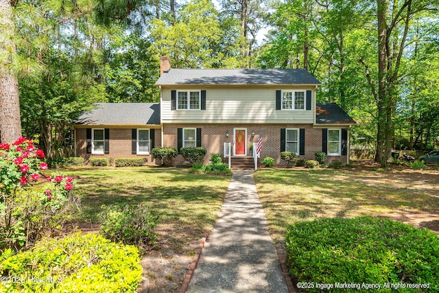 view of front of house with a chimney, brick siding, and a front lawn