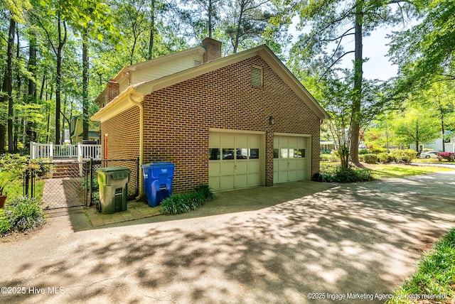 view of property exterior featuring driveway, a chimney, brick siding, and a garage