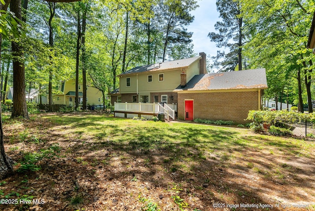 rear view of property featuring a wooden deck, a chimney, a lawn, brick siding, and fence