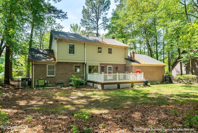 back of house featuring a deck, a chimney, brick siding, fence, and a lawn