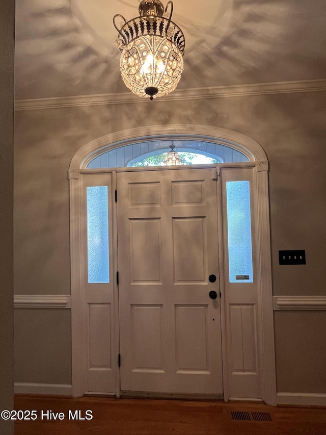 entryway featuring crown molding, visible vents, wood finished floors, and a notable chandelier