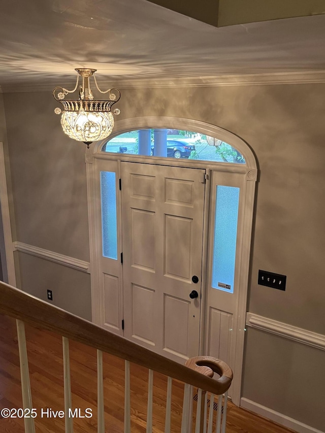 entrance foyer with crown molding, wood finished floors, and a notable chandelier