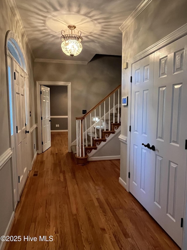 interior space with crown molding, a notable chandelier, stairs, baseboards, and wood finished floors