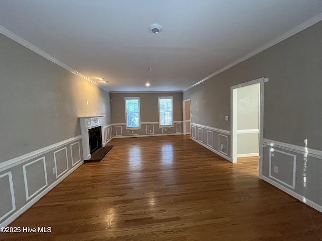 unfurnished living room with crown molding, a fireplace with raised hearth, a decorative wall, and wood finished floors