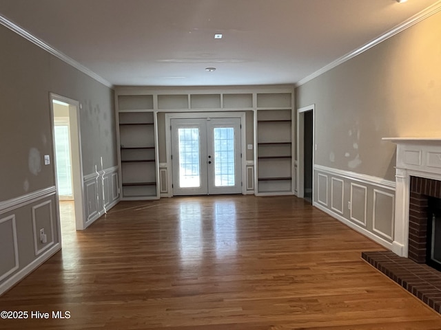 unfurnished living room featuring a brick fireplace, built in features, ornamental molding, and a decorative wall