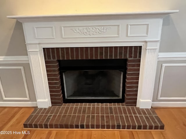 interior details with wainscoting, a brick fireplace, and wood finished floors