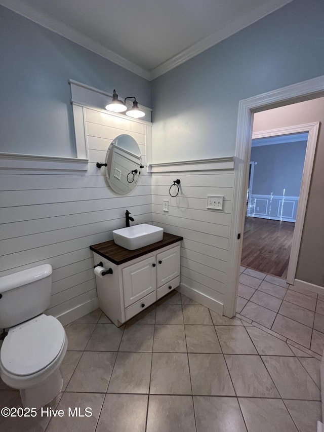 bathroom with crown molding, vanity, toilet, tile patterned floors, and a wainscoted wall